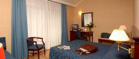 A hotel room with a bed, a desk, a chair, a lamp, and a telephone.