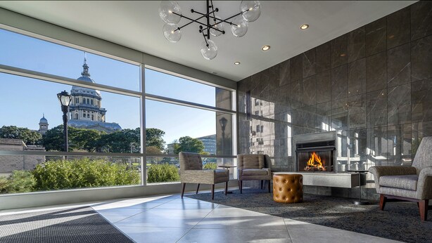 A modern lounge with a fireplace, comfortable seating, and large windows offering a city view.