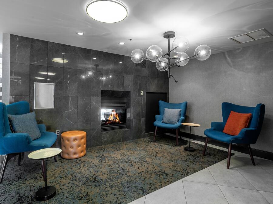 A modern lounge area with two blue armchairs, a round ottoman, a fireplace, and a unique spherical chandelier.