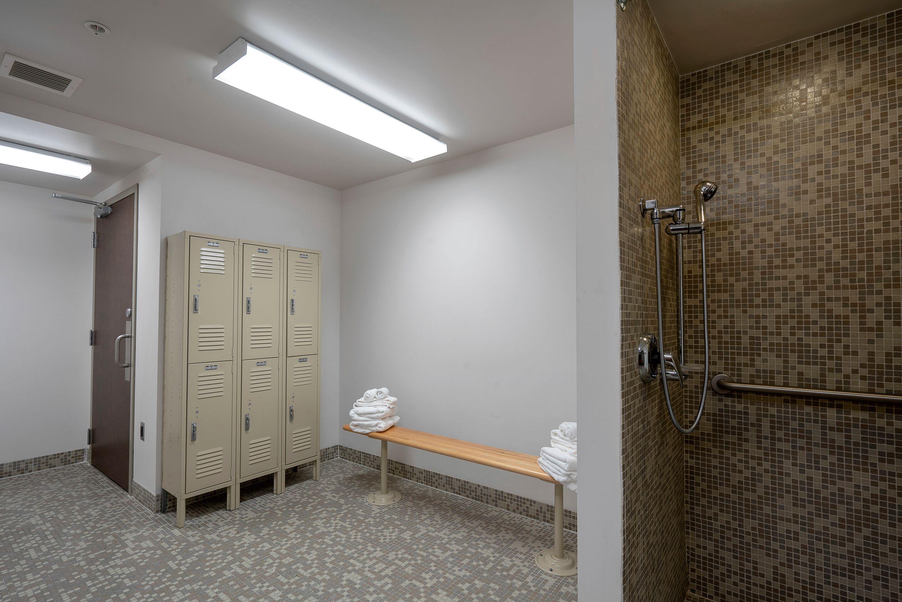 A restroom with lockers, a bench, and a shower area.