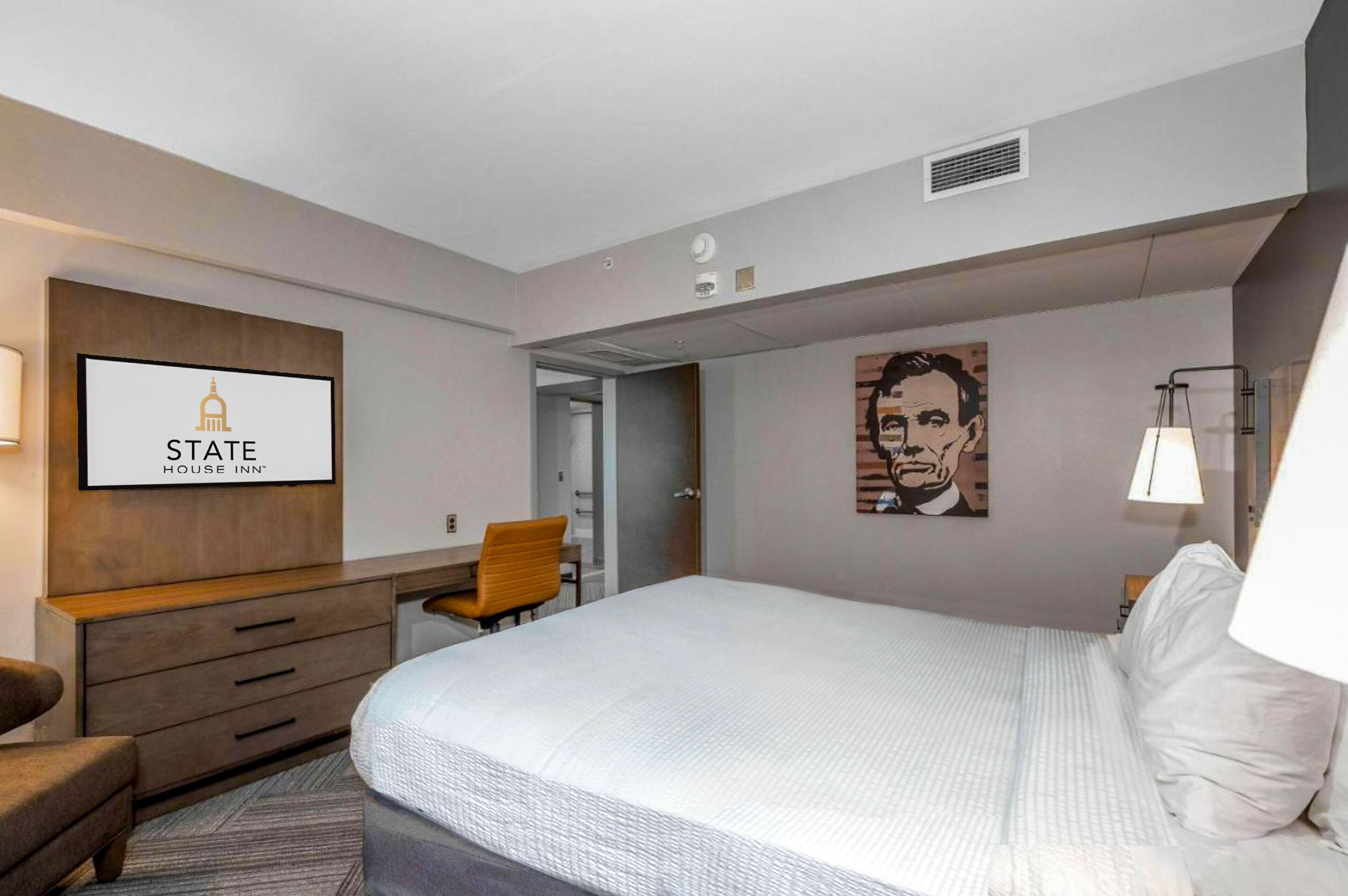 A hotel room with a bed, a desk with a chair, a television displaying "STATE HOUSE INN", and a painting on the wall.