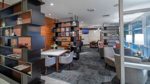 A modern hotel lobby with a dining area, a TV screen, and a large window.
