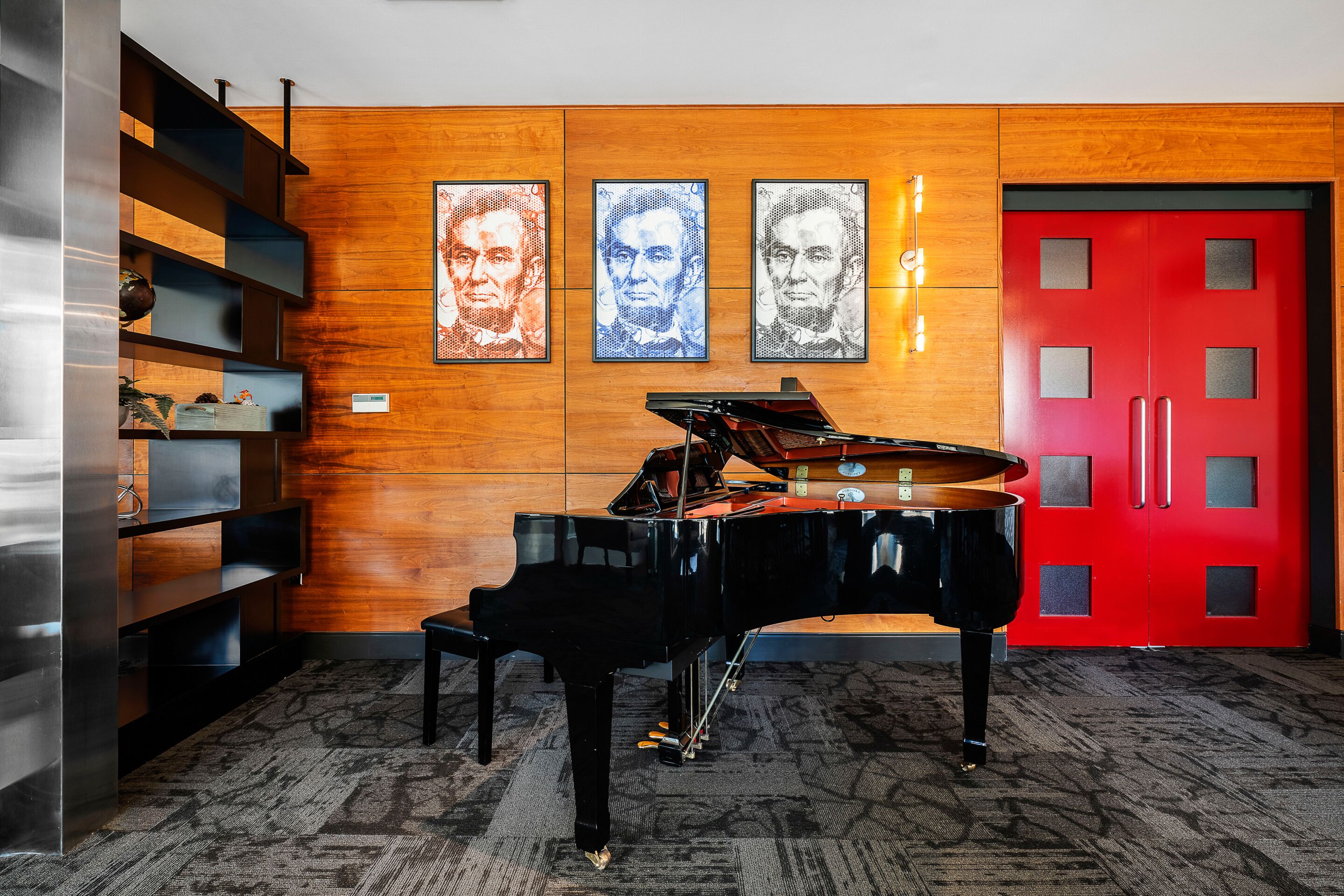A grand piano in a room with wooden paneling and a red door.