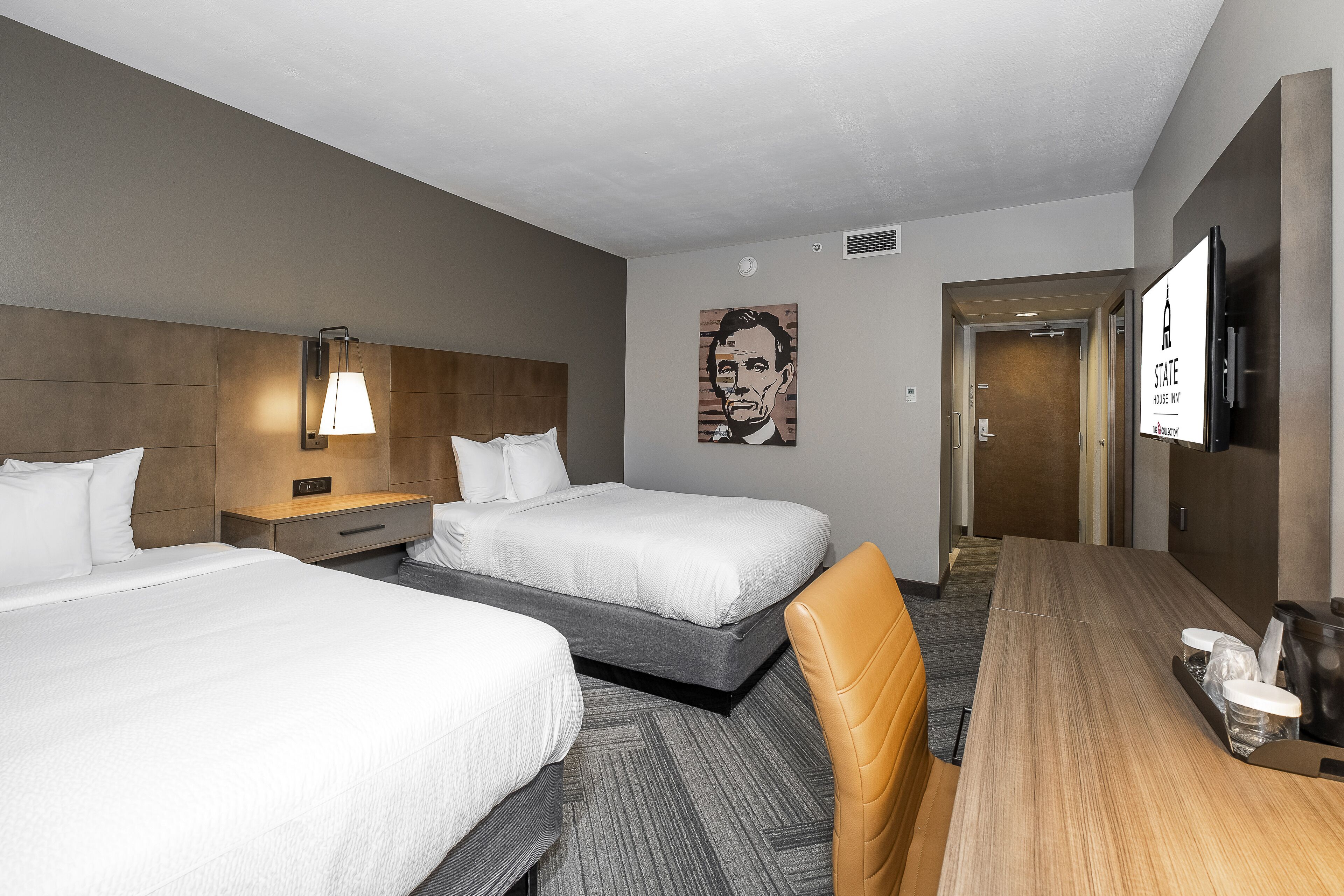 Habitación de hotel con dos camas, un escritorio, una silla, una lámpara y un televisor.