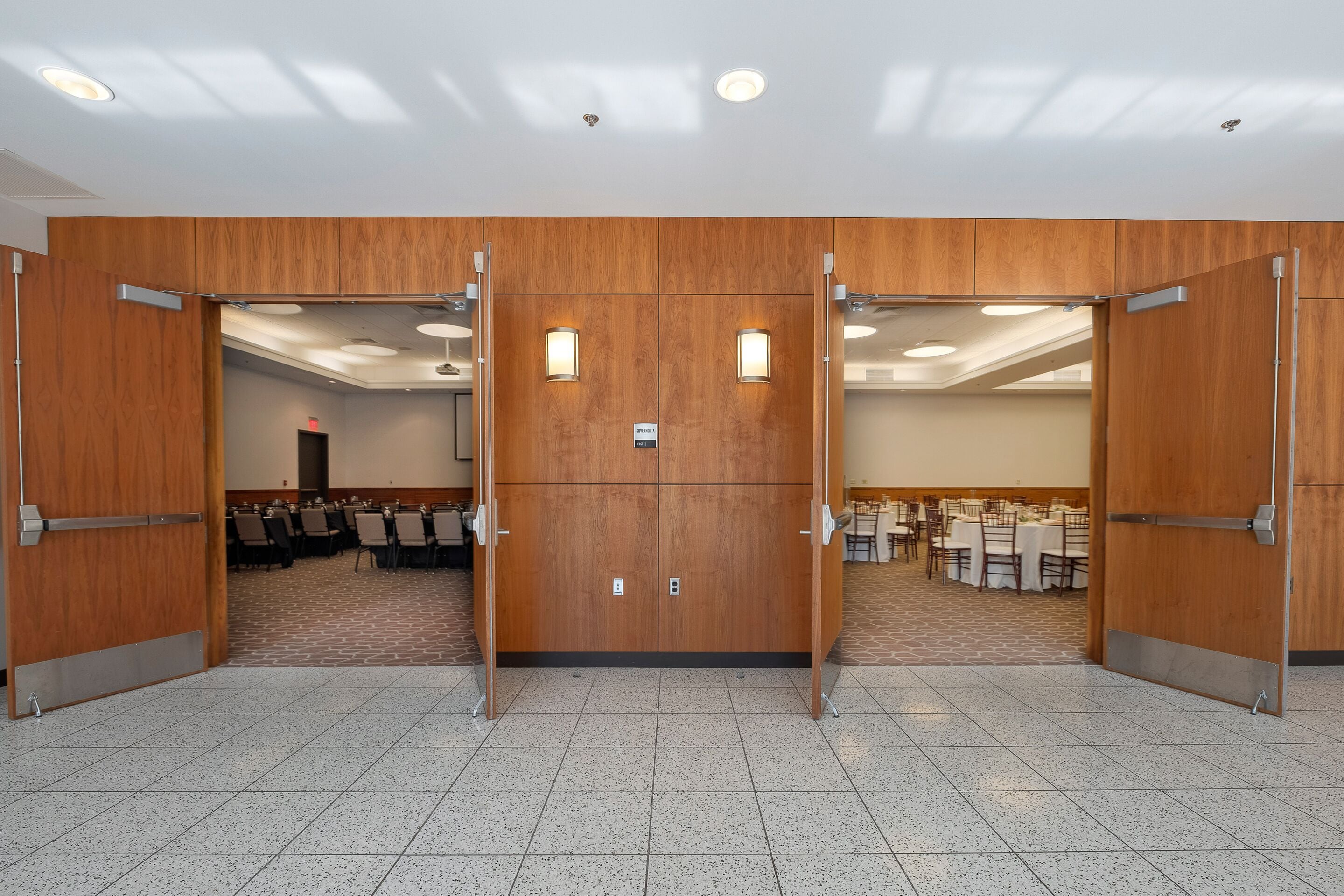 Une salle de conférence dotée d’une grande porte en bois, d’un sol carrelé et de tables disposées pour les réunions.