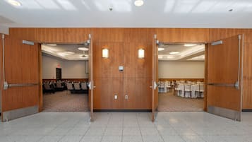Un salón de conferencias con una puerta grande de madera, suelo de baldosas y mesas dispuestas para reuniones.