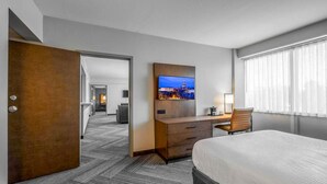 A hotel room with a bed, a desk, a television, and a view of a cityscape through the window.