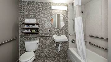 A bathroom with a toilet, sink, and shower. There are towels and toiletries on a shelf.