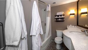 A bathroom with a bathtub, toilet, and sink. There are towels on a shelf and a shower curtain.