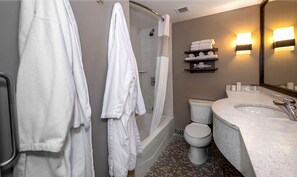 A bathroom with a bathtub, toilet, and sink. There are towels on a shelf and a shower curtain.