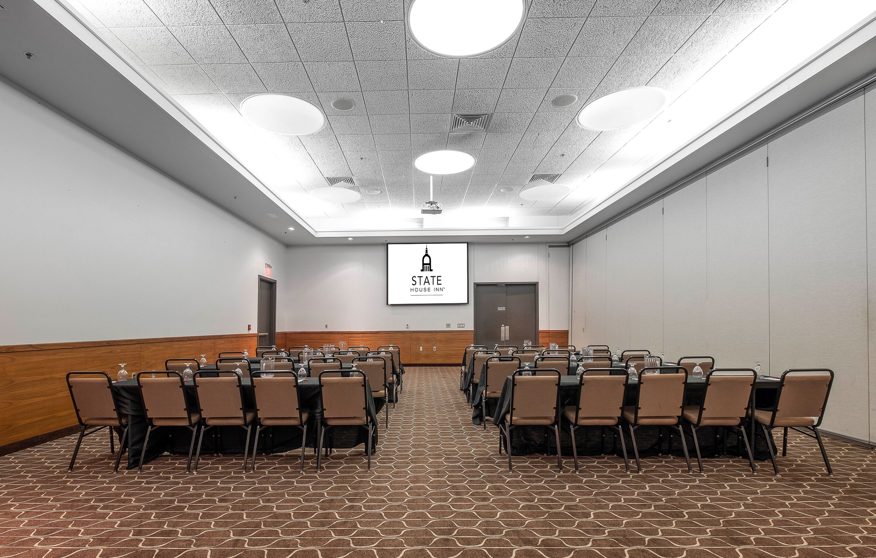 A conference room with a stage, a projector screen, and a banner reading "STATE HOUSE INN".