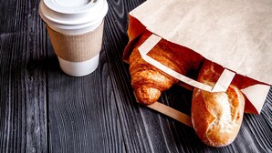 Une tasse de café et un sac en papier contenant du pain, posés sur une surface en bois.