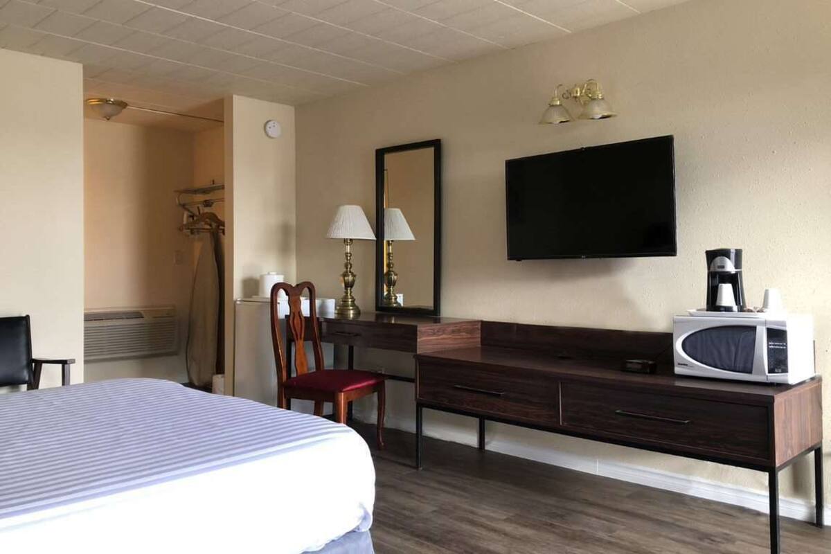 Een hotelkamer met een bed, een bureau met stoel, een televisie, een magnetron en een koffiezetapparaat.