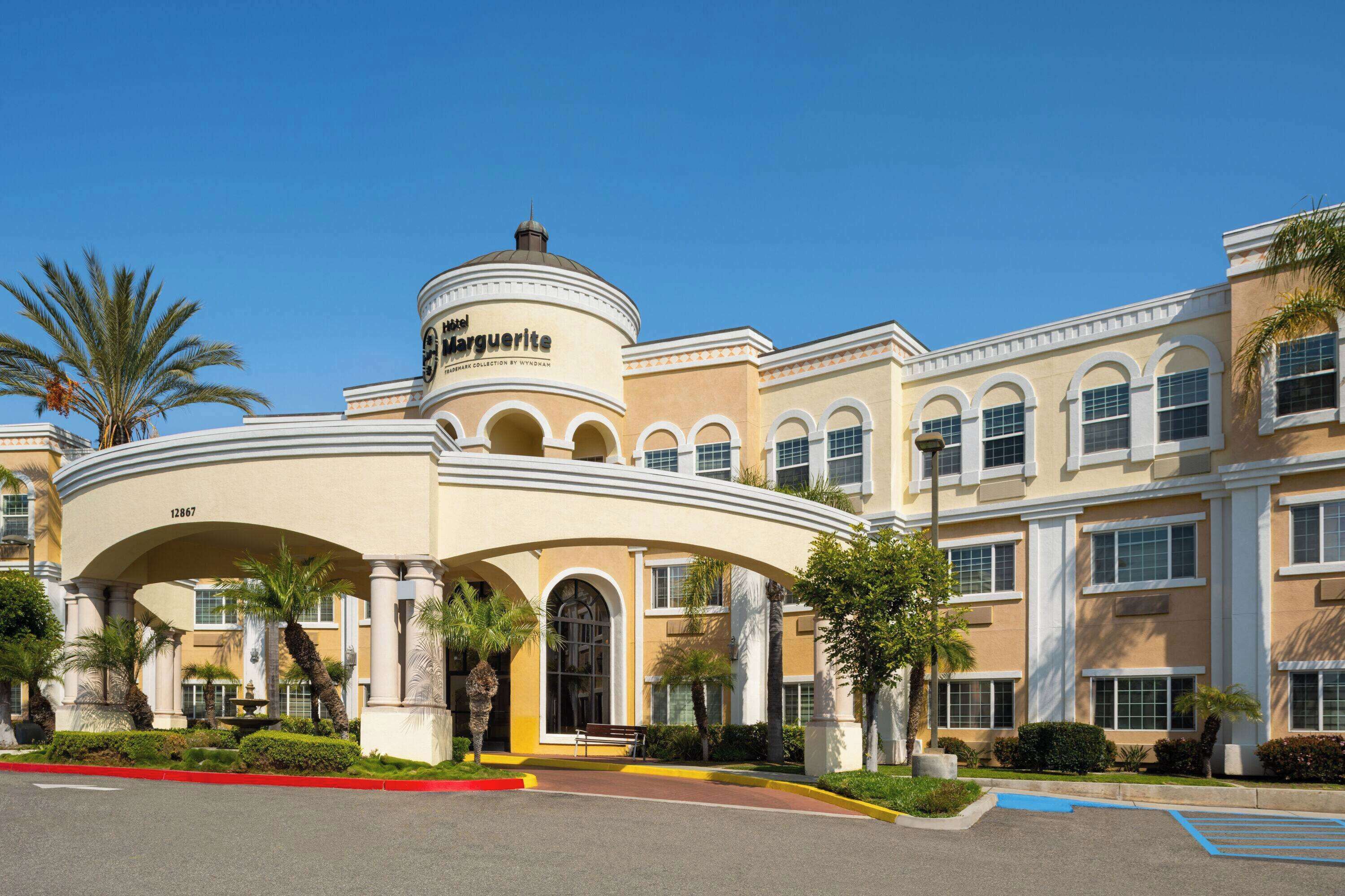 Un hôtel à la façade incurvée, bordé de palmiers, avec une fontaine dans le hall d’entrée.