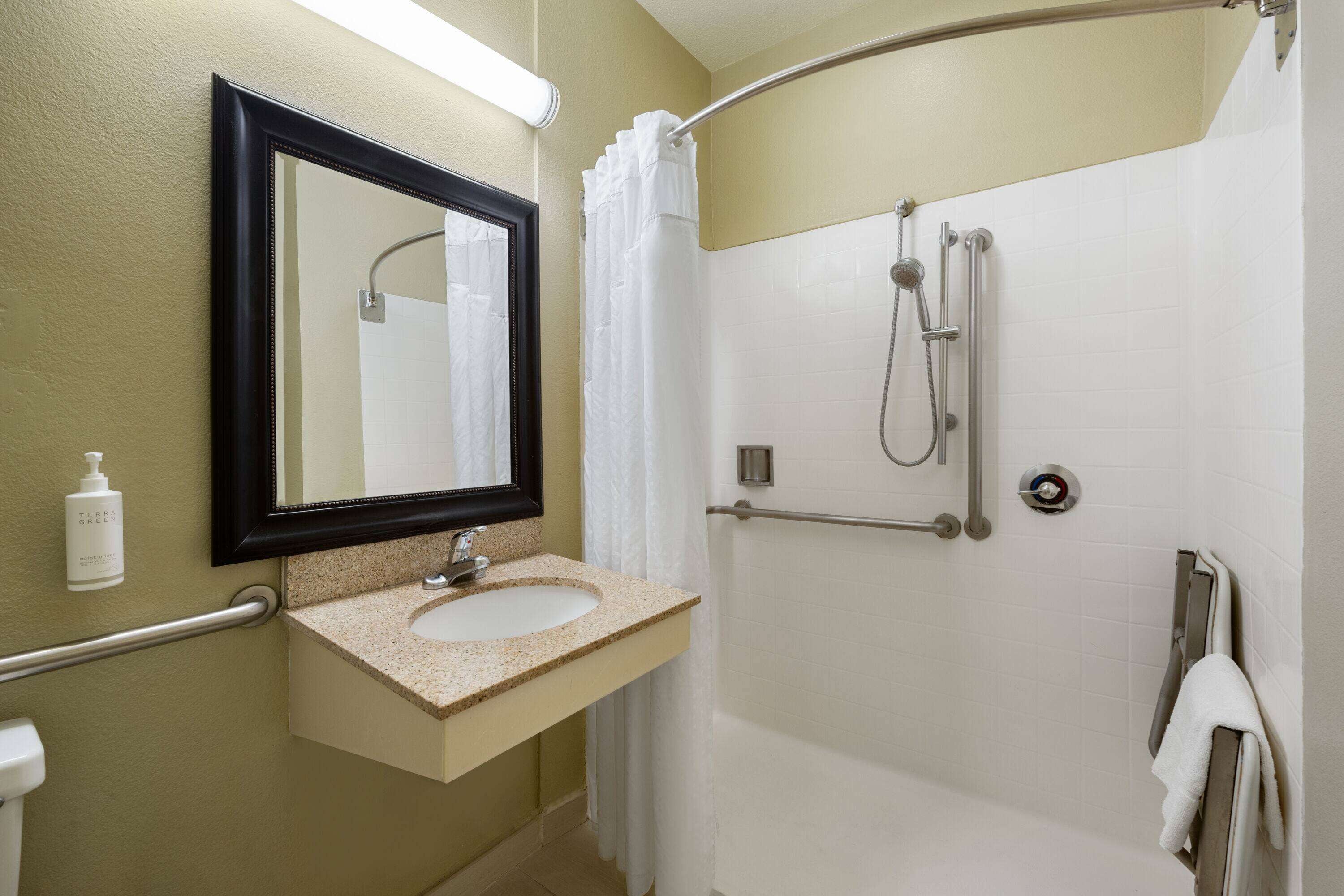 Un baño con lavamanos, espejo, ducha y toallero.