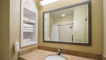 A bathroom with a granite countertop sink, a large mirror, and a towel rack with folded towels.