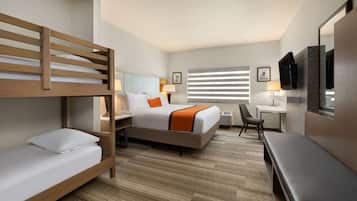 Ein Hotelzimmer mit Etagenbett, Schreibtisch, Stuhl, Bank, Fernseher und einem Fenster mit Jalousien.