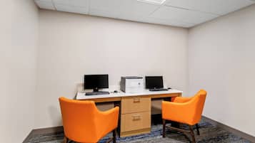 A small office with two orange chairs, a desk with two monitors, a printer, and a carpeted floor.