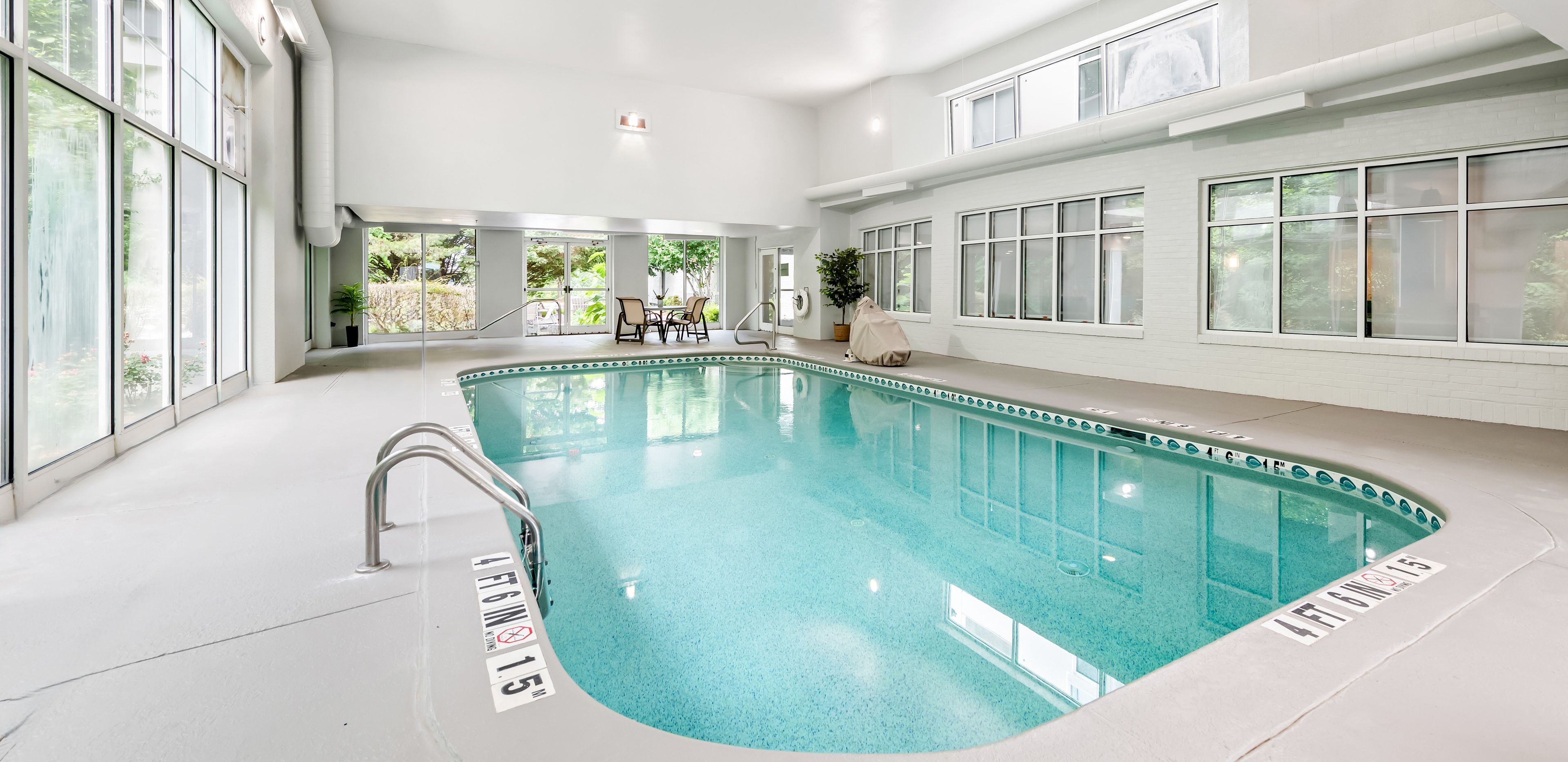 Piscina interior con señalización clara, una silla de socorrista y vistas al exterior a través de grandes ventanales.