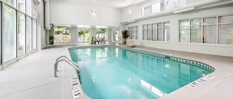 Piscina interior con señalización clara, una silla de socorrista y vistas al exterior a través de grandes ventanales.