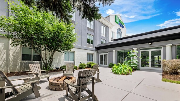 An outdoor seating area with Adirondack chairs and a fire pit, a building with a sign, and a clear sky.