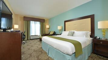 A hotel room with a large bed, two bedside tables, a desk with a chair, a television, and a window with curtains.
