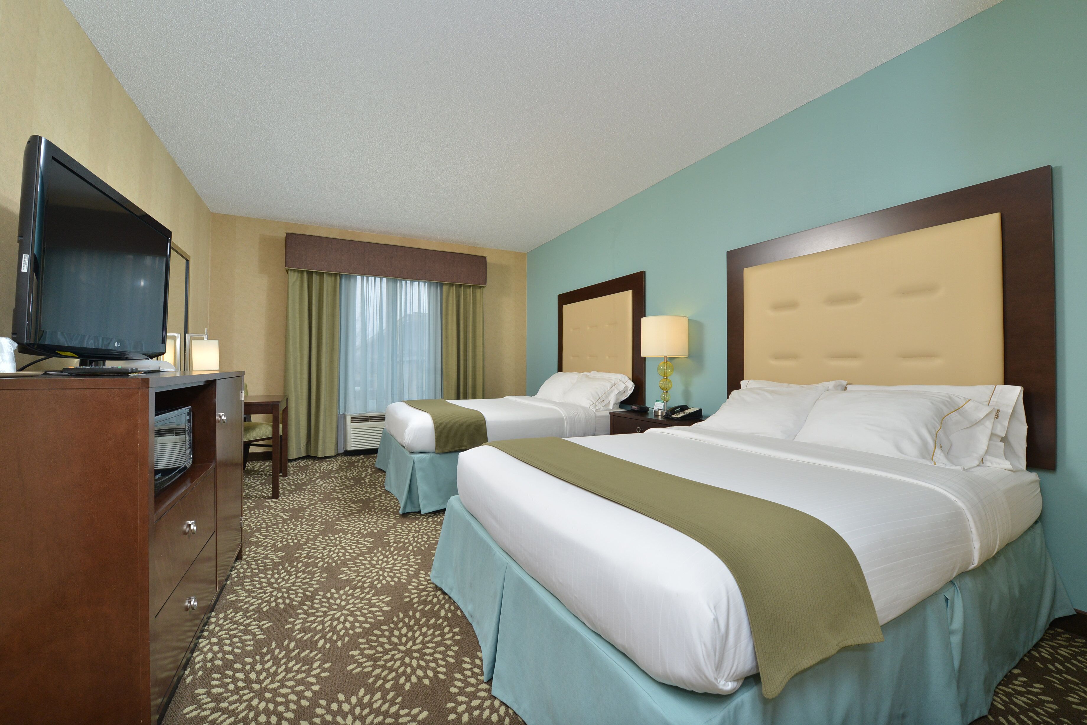 A hotel room with two beds, a desk, a television, and a window with curtains.