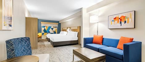Ein Hotelzimmer mit einem Bett, einem blauen Sofa mit orangefarbenen Kissen, einem Holztisch und einem blauen Sessel.