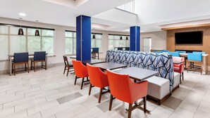 A modern dining area with high tables, orange chairs, and blue patterned booths.
