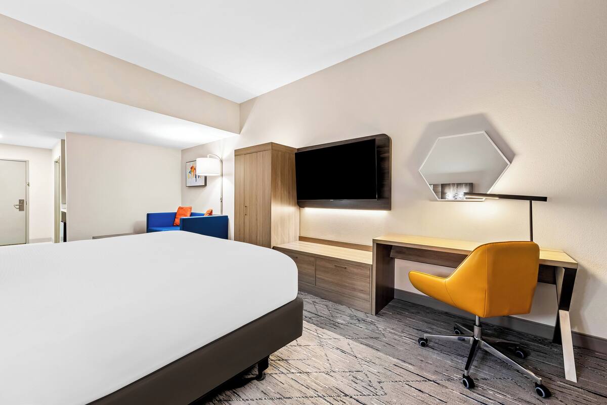 A hotel room with a large bed, a desk, a chair, a TV, and a mirror.