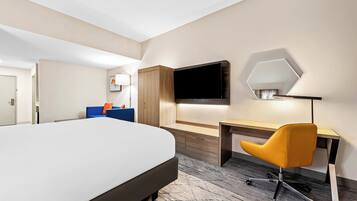 A hotel room with a large bed, a desk, a chair, a TV, and a mirror.