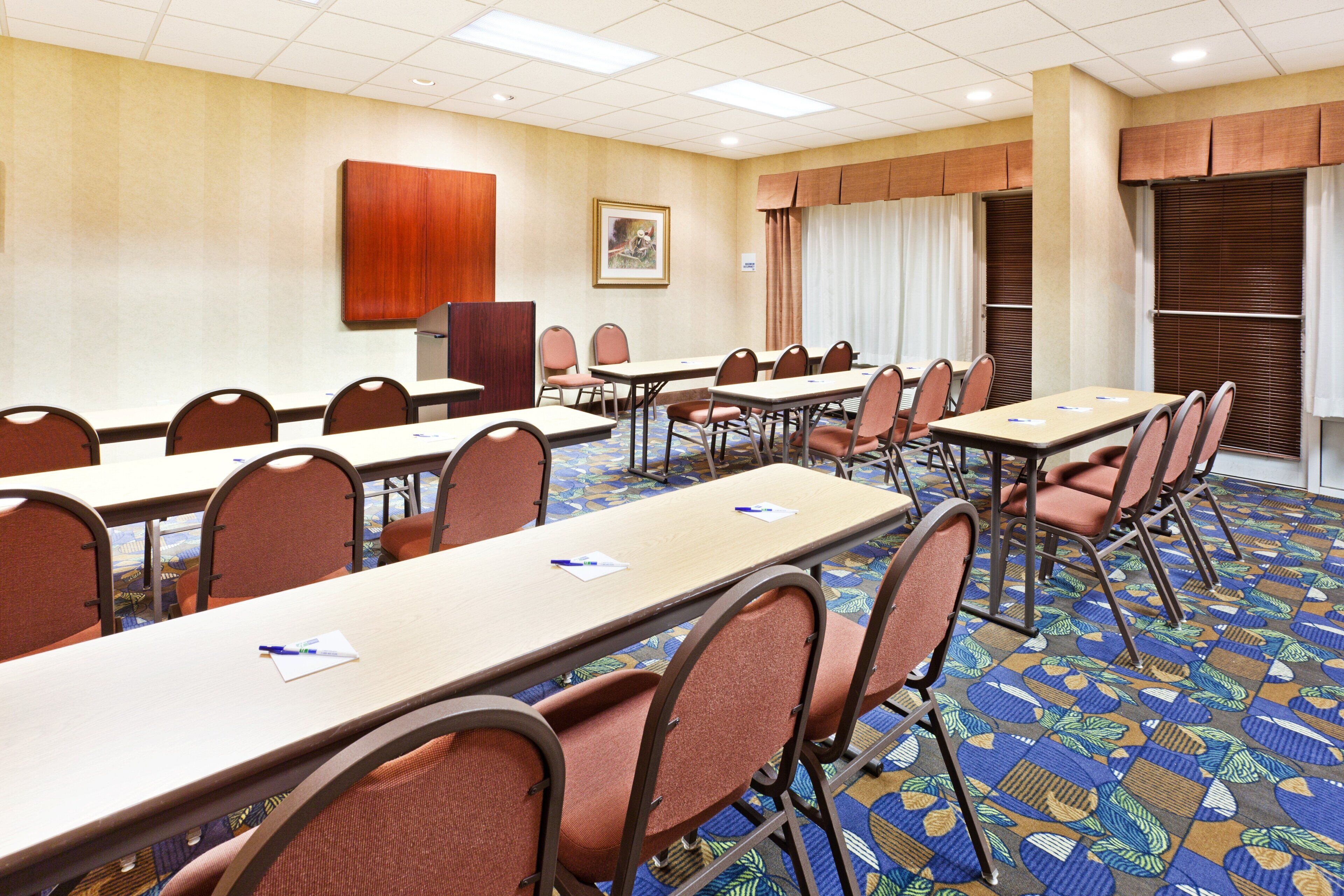 Un salón de conferencias con varias mesas y sillas, un armario de madera y una alfombra estampada.