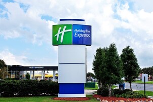 A Holiday Inn Express sign with a blue and green logo, surrounded by greenery and a parking lot.