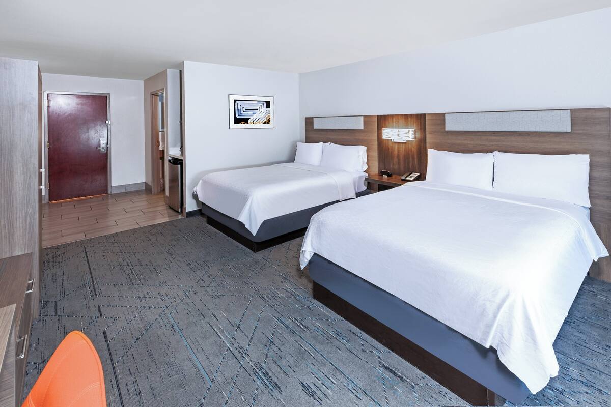 A hotel room with two beds, a wooden headboard, a desk with a phone, and a door leading to a bathroom.