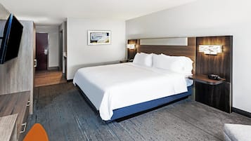 Una moderna camera d'hotel con un letto grande, una televisione a schermo piatto, una testiera in legno e un tavolino con una lampada.