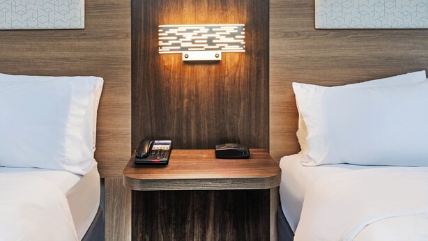 A hotel room with two beds, a nightstand with a phone and a portable charger, and a wall-mounted light fixture. - Holiday Inn Express Harvey-Marrero by IHG (Harvey)