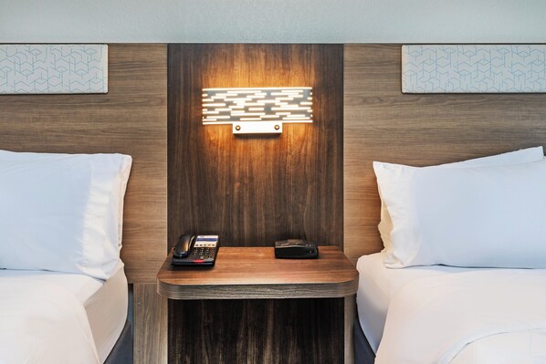 Habitación de hotel con dos camas, una mesita de noche con un teléfono y un cargador portátil, y un aplique de pared.