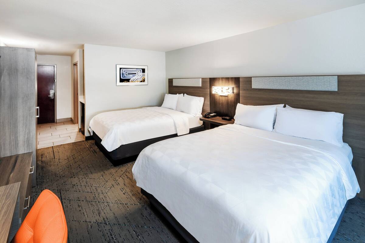 A hotel room with two beds, a desk, and a chair.