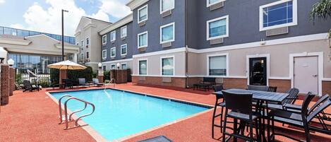 A hotel with a swimming pool, outdoor seating, and a brick facade.