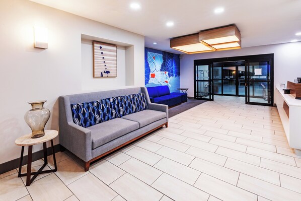 A modern lobby with a grey sofa, a vase on a small table, and a map on the wall. - Holiday Inn Express Harvey-Marrero by IHG (Harvey)