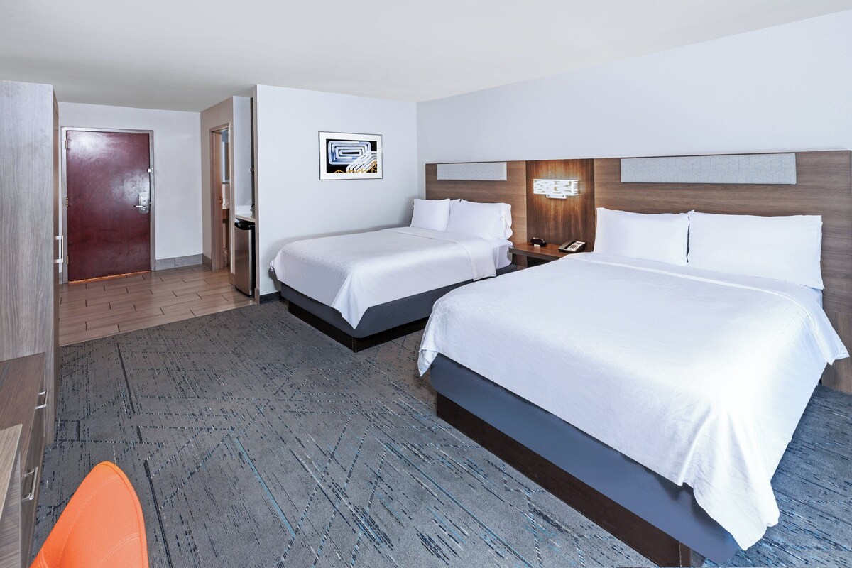 A hotel room with two beds, a wooden headboard, a desk with a phone, and a door leading to a bathroom.