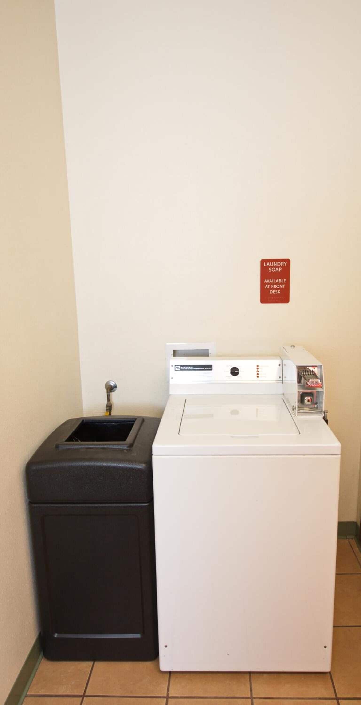 A front-loading washing machine and a black trash bin in a hotel room.