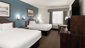 A hotel room with two beds, a desk, a TV, and a window with curtains. - Tombstone Grand Hotel, a Baymont by Wyndham (Tombstone)