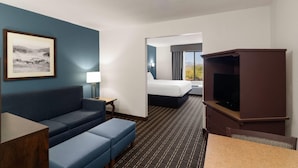 Habitación de hotel con sofá azul, televisor, cama y un cuadro en la pared.