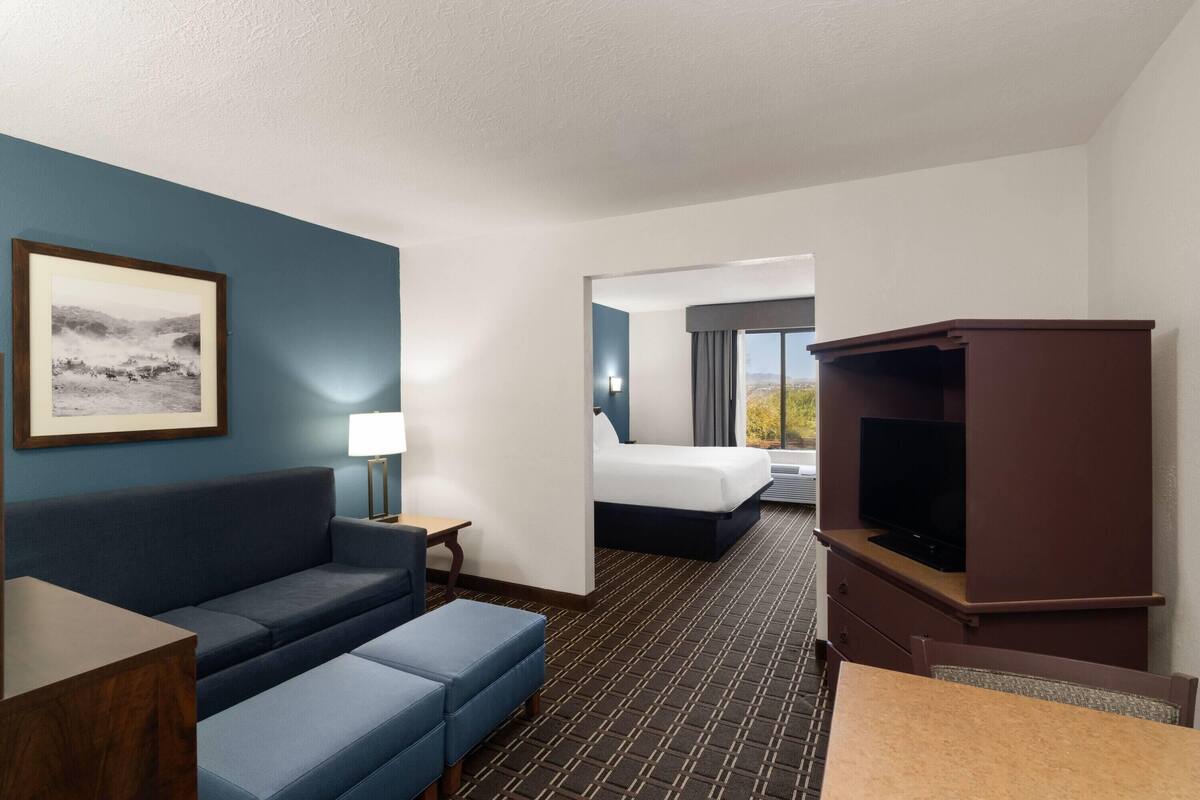 A hotel room with a blue sofa, a TV, a bed, and a framed picture on the wall.