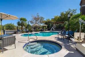 A swimming pool with a hot tub, lounge chairs, and umbrellas.