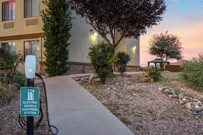 An electric vehicle charging station with a sign, a pathway, and a building with a stone facade and windows.