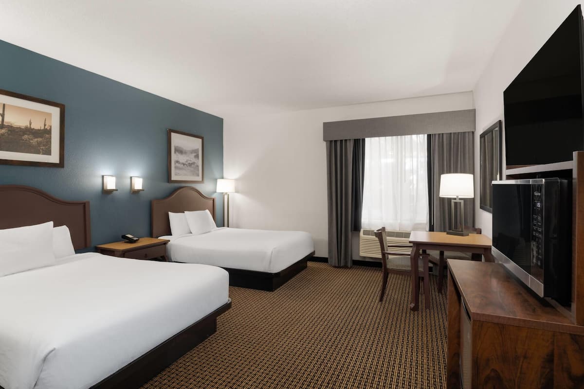 A hotel room with two beds, a desk, a TV, and two wall-mounted lamps.