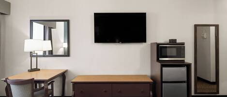 Una habitación de hotel con cama, escritorio con lámpara, televisión, microondas y minibar.