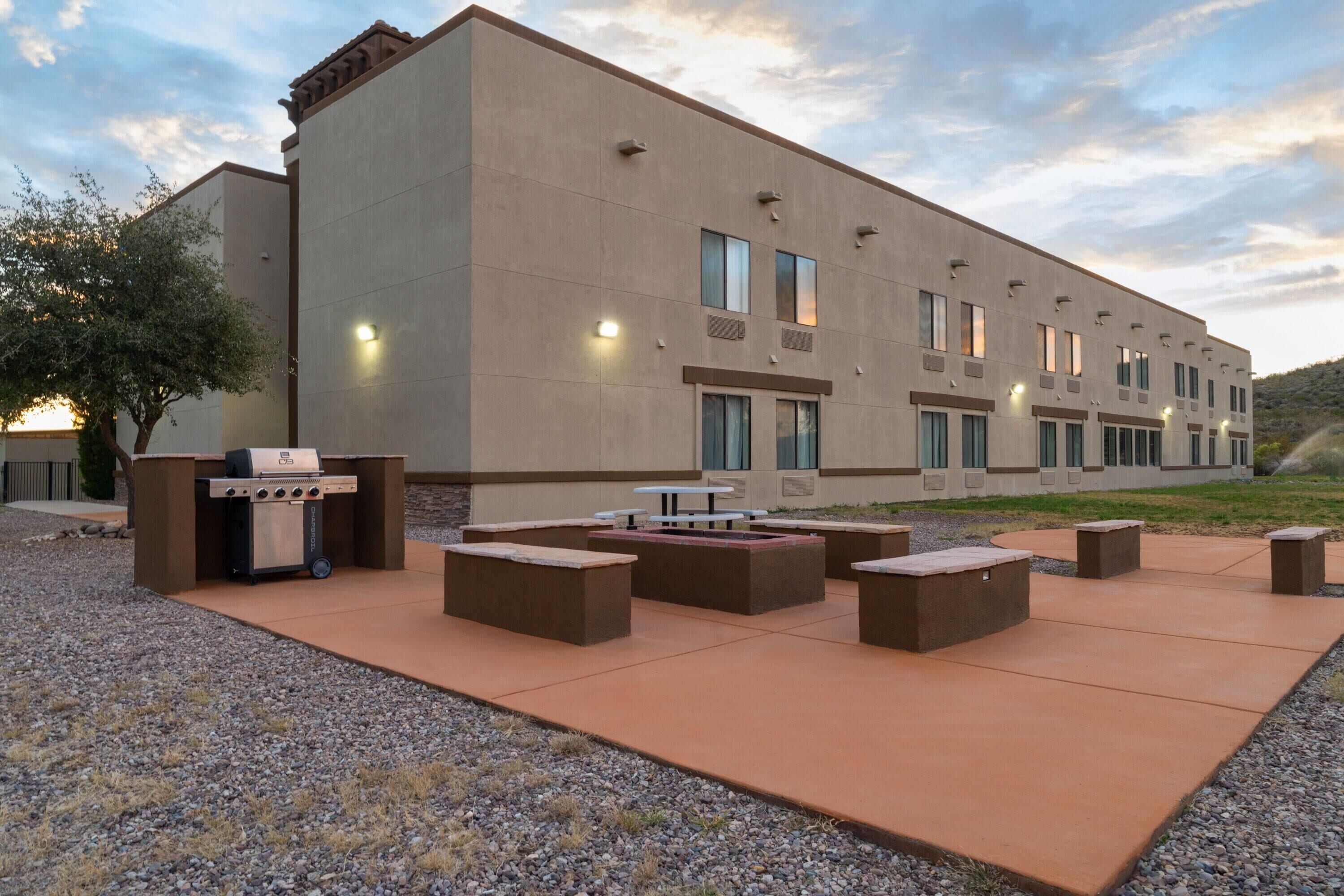 An outdoor patio area with a barbecue grill, seating, and a building with multiple windows.